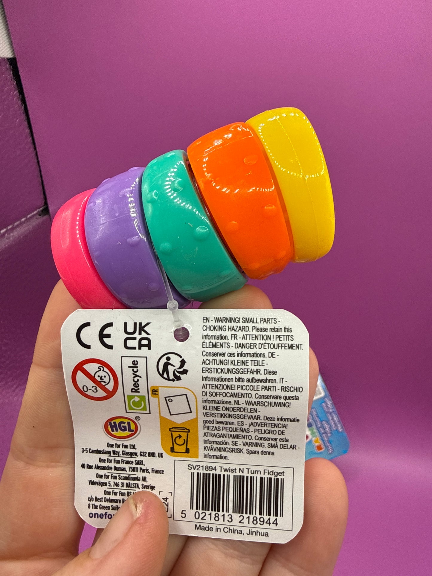 Colorful 'Twist 'n Turn' rainbow fidgets with packaging on a pink background